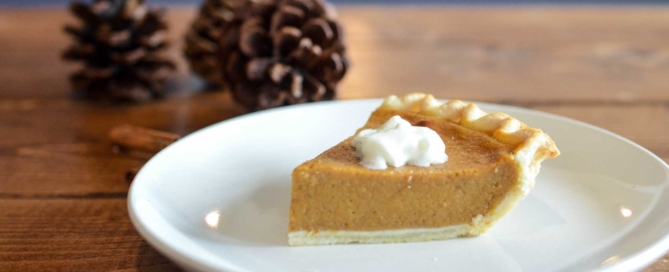 A piece of pie on a wooden table with pine cones in the background